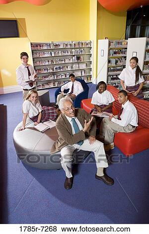 Stock Photo - Group of high school students hanging out in library with teacher. Fotosearch