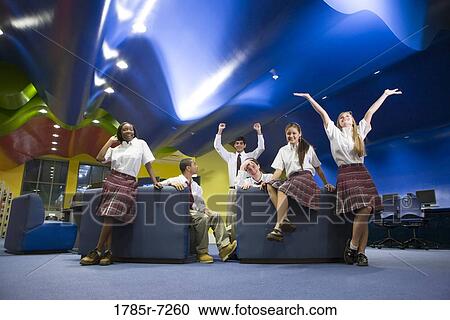 Stock Image - Group of teenage students hanging out in lounge area of library. Fotosearch