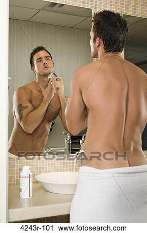 Stock Image - Handsome male fitness athlete shaving in front of bathroom mirror in towel. Fotosearch