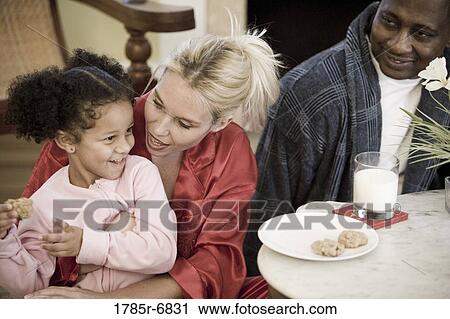 Inter-racial family with young daughter dressed in pajamas sitting in living room View Large Photo Image Stock Image - Inter-racial family with young daughter dressed in pajamas sitting in living room. Fotosearch