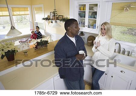 Interracial couple in then kitchen with children in background View Large Photo Image Stock Photo - Interracial couple in then kitchen with children in background. Fotosearch
