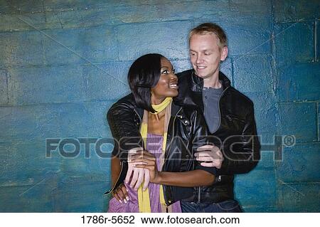Stock Image - Interracial couple leaning against grungy blue wall. Fotosearch