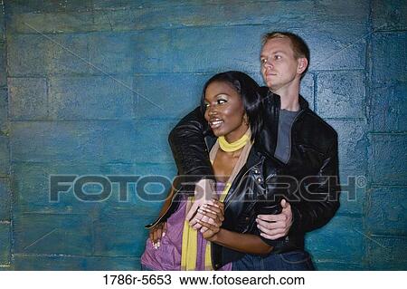 Stock Image - Interracial couple leaning against grungy blue wall. Fotosearch