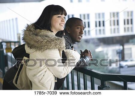 Interracial couple leaning against railing overlooking city street View Large Photo Image Stock Photo - Interracial couple leaning against railing overlooking city street. Fotosearch