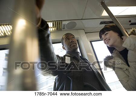 Low angle view of a cheerful young inter-racial couple traveling in a mass transit train View Large Photo Image Picture - Low angle view of a cheerful young inter-racial couple traveling in a mass transit train. Fotosearch