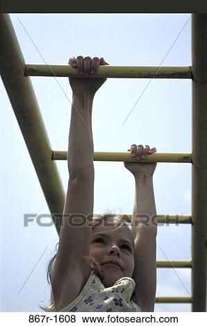 Stock Photo - Low angle view of a girl hanging on monkey bars. Fotosearch