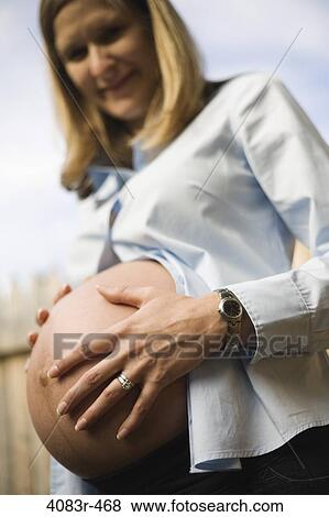 Stock Photo - Low angle view of a pregnant woman touching her abdomen. Fotosearch