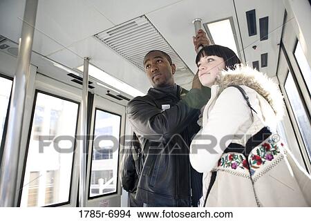 Low angle view of a young inter-racial couple traveling in a mass transit train View Large Photo Image Picture - Low angle view of a young inter-racial couple traveling in a mass transit train. Fotosearch