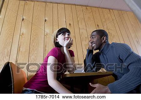 Low angle view of a young inter-racial couple sitting in a cafe View Large Photo Image Picture - Low angle view of a young inter-racial couple sitting in a cafe. Fotosearch
