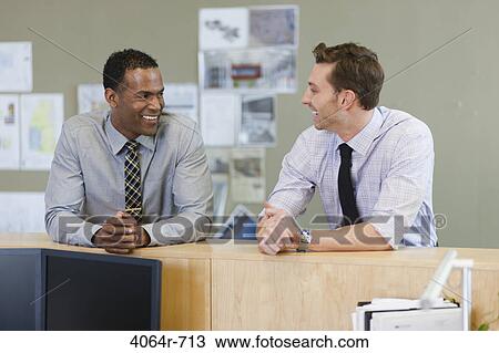 Stock Image - Male co-workers hanging out at office. Fotosearch