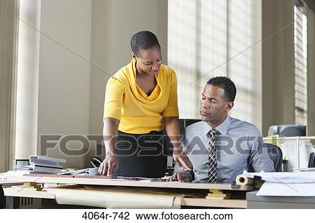 Stock Image - Man and woman consulting at desk in office. Fotosearch