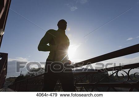 Stock Photo - Man jogging, backlit by sun. Fotosearch