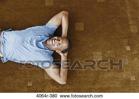 Stock Image - Man relaxing on floor in loft apartment. Fotosearch