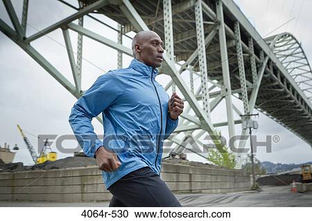 Stock Image - Man running underneath bridge. Fotosearch