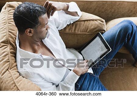 Man sitting on couch with ebook View Large Photo Image Stock Image - Man sitting on couch with ebook. Fotosearch