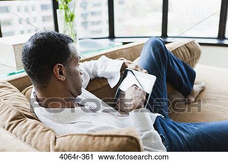 Man sitting on couch with ebook View Large Photo Image Stock Image - Man sitting on couch with ebook. Fotosearch