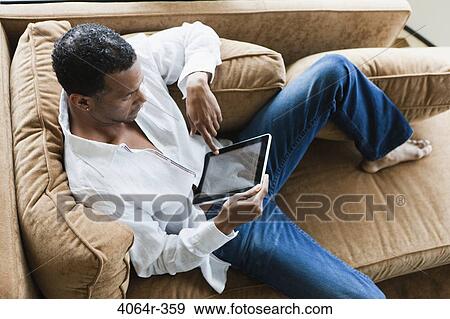 Man sitting on couch with ebook View Large Photo Image Stock Photo - Man sitting on couch with ebook. Fotosearch