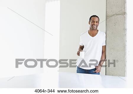 Man standing with coffee cup in loft apartment View Large Photo Image Picture - Man standing with coffee cup in loft apartment. Fotosearch