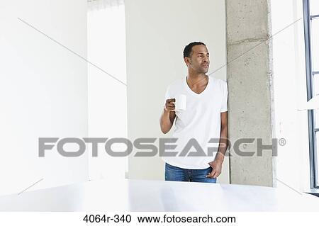 Stock Image - Man standing with coffee cup in loft apartment. Fotosearch
