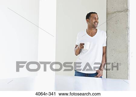 Stock Image - Man standing with coffee cup in loft apartment. Fotosearch