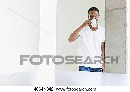 Stock Image - Man standing with coffee cup in loft apartment. Fotosearch