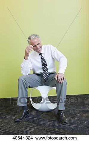 Mature businessman sitting on designer chair against yellow background View Large Photo Image Picture - Mature businessman sitting on designer chair against yellow background. Fotosearch