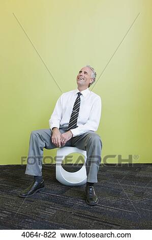 Mature businessman sitting on designer chair against yellow background, laughing View Large Photo Image Stock Image - Mature businessman sitting on designer chair against yellow background, laughing. Fotosearch
