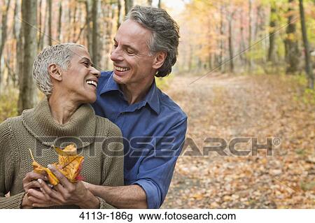 Stock Image - Mature couple holding Autumn leaves in forest. Fotosearch
