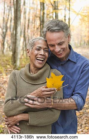 Stock Image - Mature couple holding Autumn leaves in forest. Fotosearch