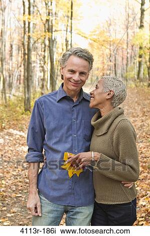 Stock Image - Mature couple holding Autumn leaves in forest. Fotosearch