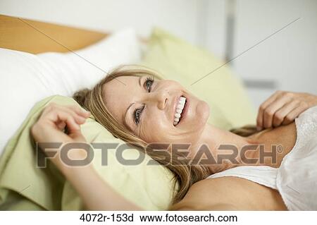 Stock Image - Mature woman day dreaming and smiling on the bed. Fotosearch