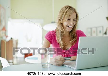 Stock Image - Mature woman doing online shopping and laughing. Fotosearch