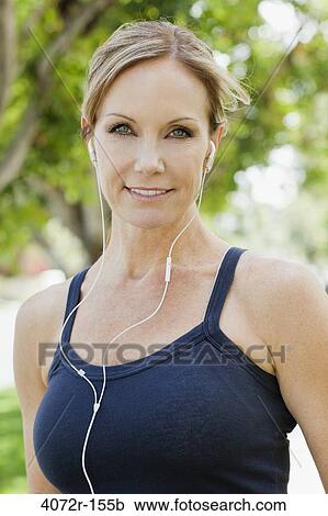 Stock Image - Mature woman listening to music with earbuds in a park. Fotosearch