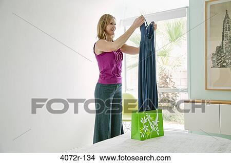 Picture - Mature woman looking at a dress and smiling at home. Fotosearch