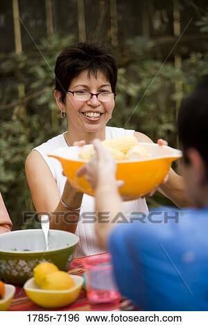 Stock Photograph - Mature woman passing a bowl of food at picnic table. Fotosearch