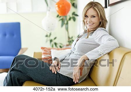 Mature woman sitting on a couch and smiling View Large Photo Image Stock Image - Mature woman sitting on a couch and smiling. Fotosearch