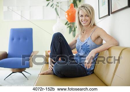 Mature woman sitting on a couch and smiling View Large Photo Image Stock Image - Mature woman sitting on a couch and smiling. Fotosearch