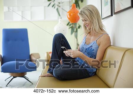 Mature woman sitting on a couch and text messaging View Large Photo Image Stock Image - Mature woman sitting on a couch and text messaging. Fotosearch