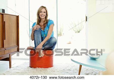 Mature woman sitting on an ottoman and smiling View Large Photo Image Stock Image - Mature woman sitting on an ottoman and smiling. Fotosearch