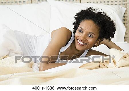 Stock Photograph - Mid adult woman lying on the bed and smiling. Fotosearch