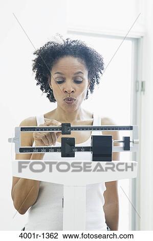 Mid adult woman measuring her weight on a weighing scale View Large Photo Image Stock Image - Mid adult woman measuring her weight on a weighing scale. Fotosearch