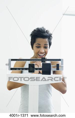 Mid adult woman measuring her weight on a weighing scale View Large Photo Image Stock Image - Mid adult woman measuring her weight on a weighing scale. Fotosearch
