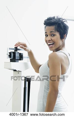 Mid adult woman measuring her weight on a weighing scale View Large Photo Image Stock Photo - Mid adult woman measuring her weight on a weighing scale. Fotosearch