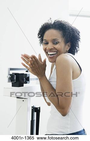 Stock Photography - Mid adult woman measuring her weight on a weighing scale. Fotosearch