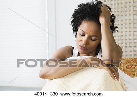 Stock Image - Mid adult woman sitting on the bed and suffering from a headache. Fotosearch