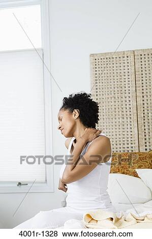 Stock Photo - Mid adult woman sitting on the bed and suffering from backache. Fotosearch