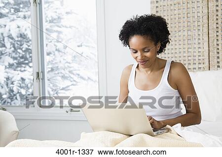 Mid adult woman sitting on the bed and using a laptop View Large Photo Image Stock Photo - Mid adult woman sitting on the bed and using a laptop. Fotosearch