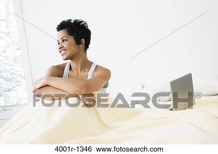 Stock Photograph - Mid adult woman sitting on the bed. Fotosearch