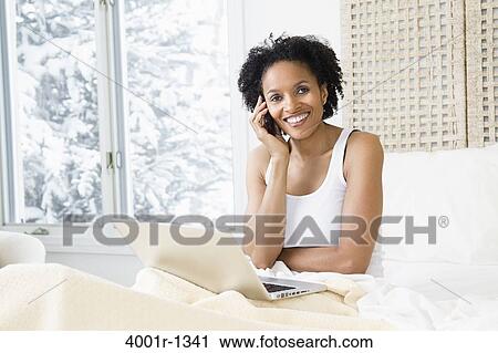 Stock Image - Mid adult woman using a laptop and talking on a mobile phone. Fotosearch