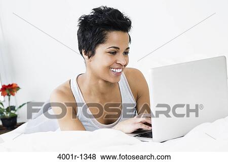 Stock Photo - Mid adult woman using a laptop on the bed. Fotosearch